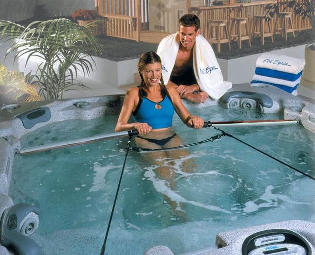 College-aged couple enjoying a swim together in a swim spa. woman in pool and man outside it.