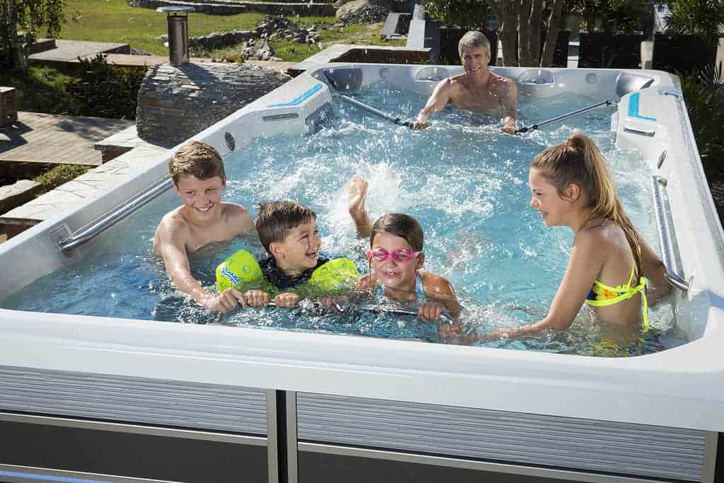 Four young kids, two boys and two girls, happily using hte swim feature in a swim spa, splashing and playing together in the water