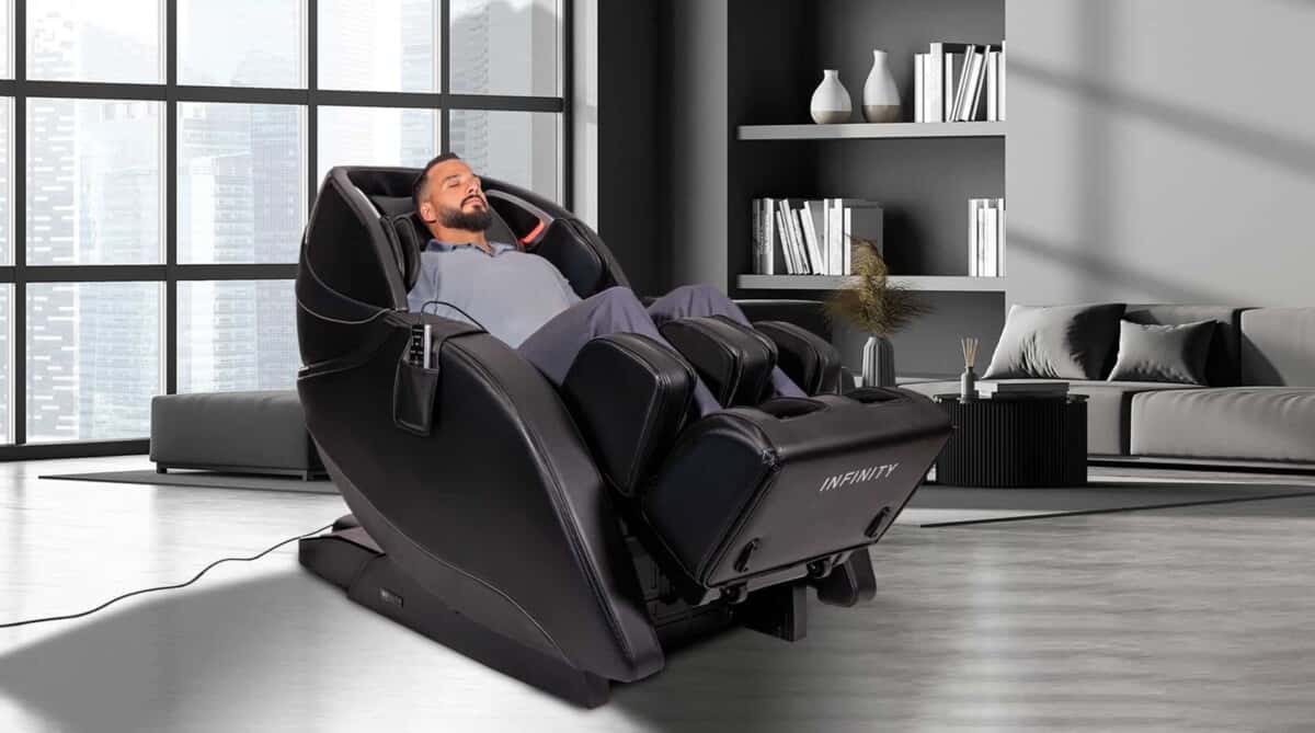 A relaxed man enjoying the benefits of a massage chair in a modern home, with a bookshelf on one side and a city skyline visible in the background.