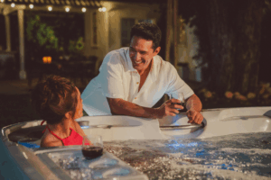 Man Getting Into A Hot Tub With A Woman In The Evening, Showcasing Sleep Benefits Of A Nightly Soak.