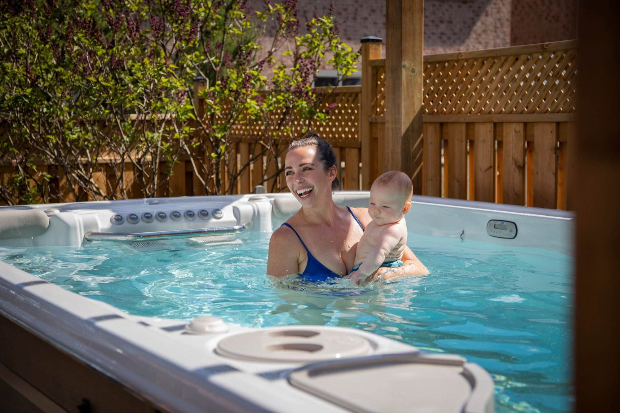 Mother and toddler together in background enjoying Hydropool Swim Spa, smiling and creating family memories, with spa side visible in foreground