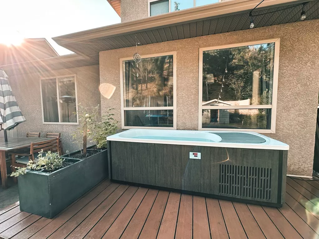 Side view of a brown and white Kodiak Cold Plunge filled with water in a backyard, with house windows visible in the background