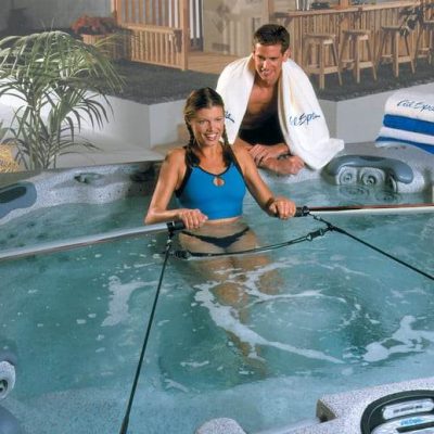 College-Aged Couple Enjoying A Swim Together In A Swim Spa. Woman In Pool And Man Outside It.