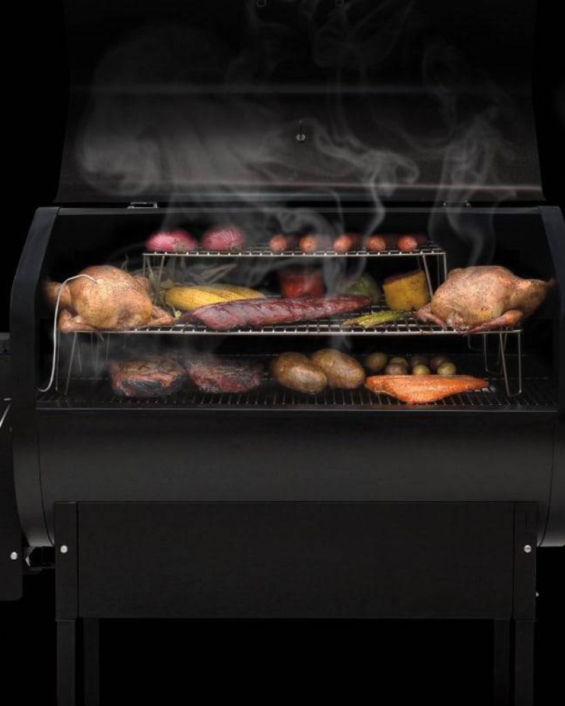 Open Green Mountain pellet grill showcasing a variety of grilled foods, set against a black background.